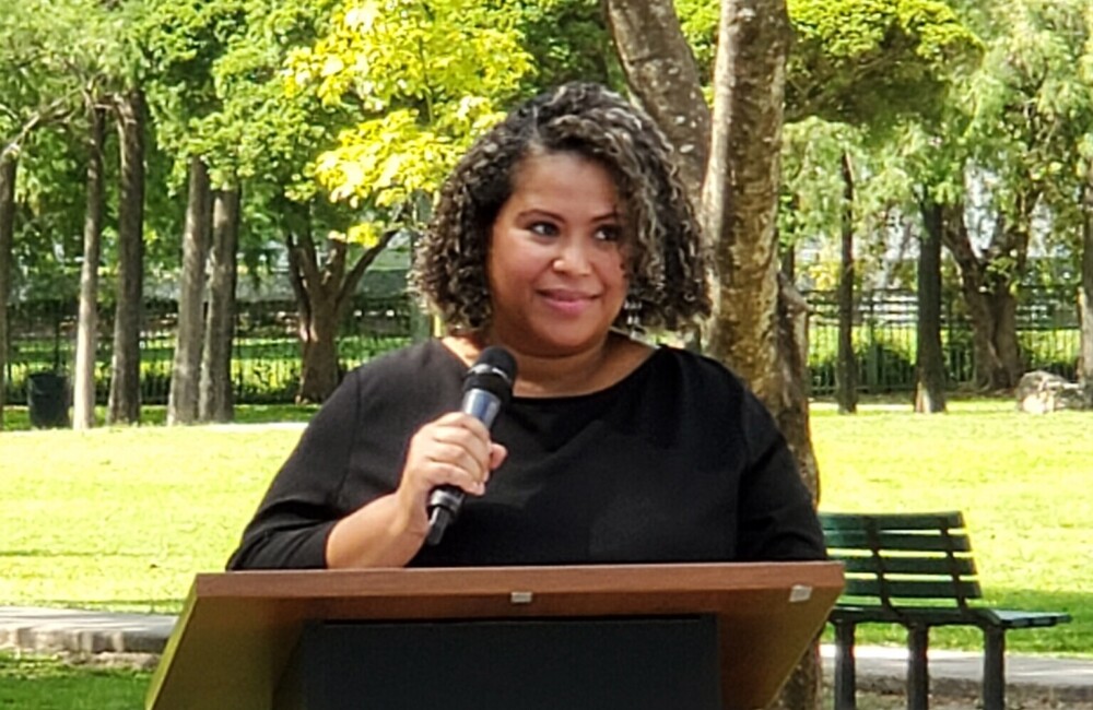 Woman holding a microphone and speaking from behind a podium.