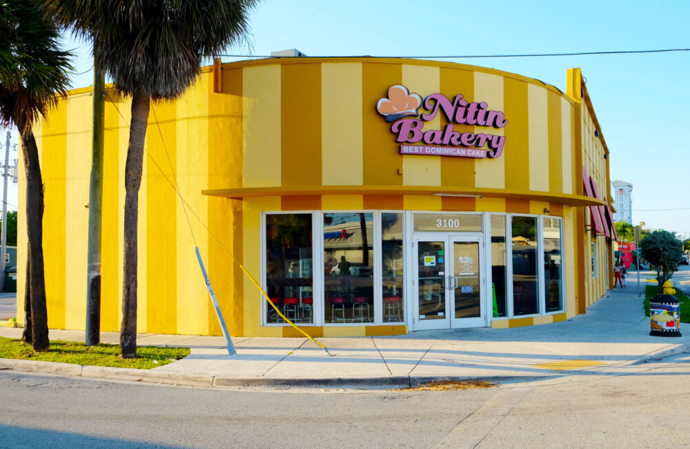 A bakery shop with a curved exterior, large floor-to-ceiling windows, and a brightly painted facade of yellow and ochre vertical stripes.