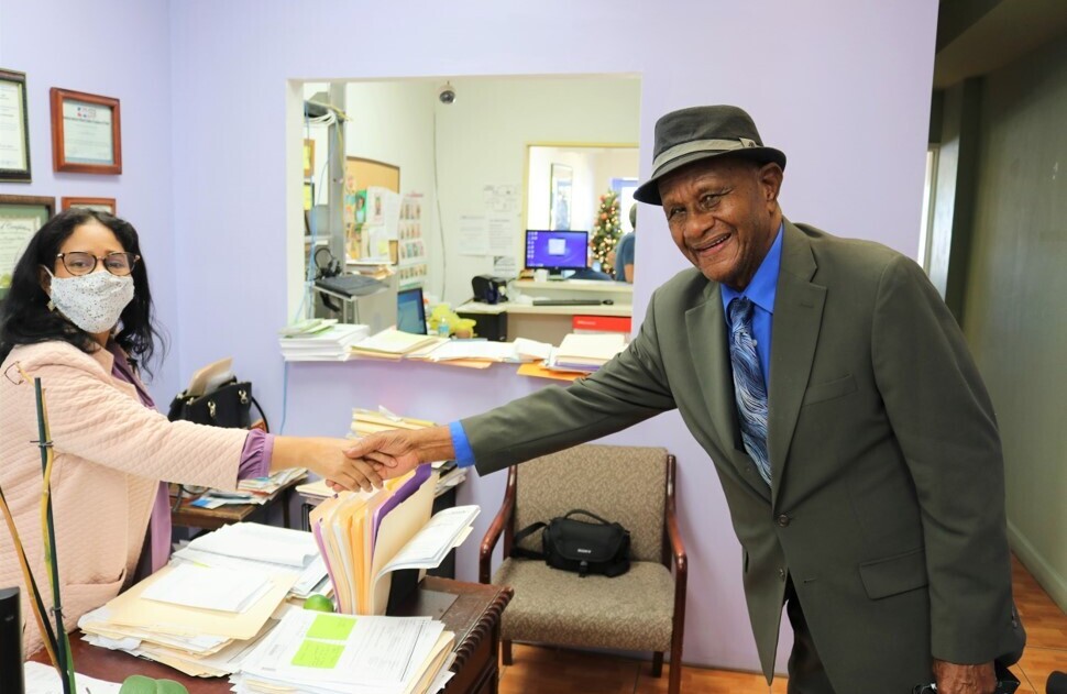 A woman and a man reach across a desk to shake hands.