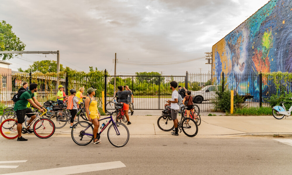 People on bikes gather in front of a mural.