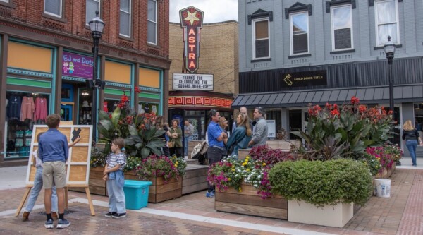 People gather in a town square surrounded by historic buildings.