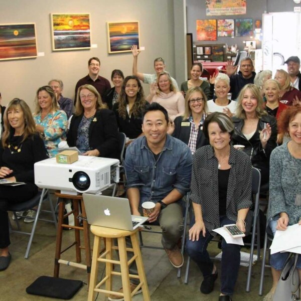 Large group of people gathered in an office space smiling at the camera in front of a projector.