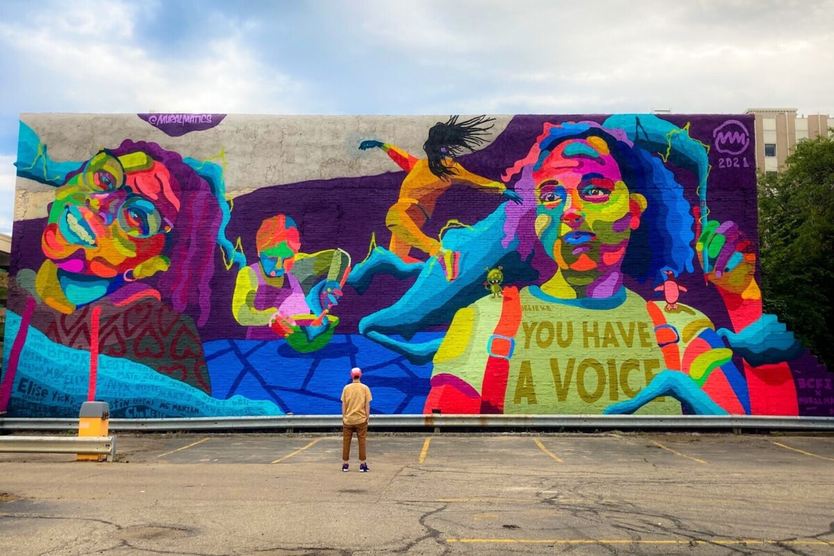 A person stands in front of a large colorful mural.