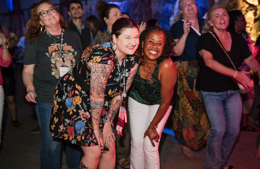 Two women pose for a photo while people dance around them.