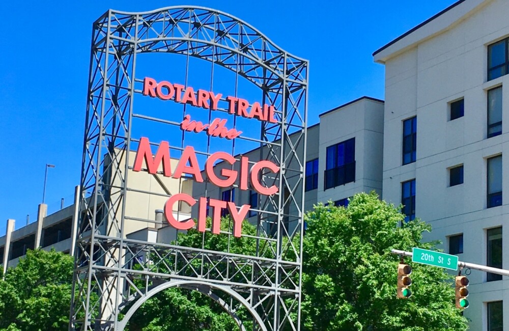 People enjoying a peddle tour through Birmingham while passing a large sign displaying the words "Rotary Trail in the Magic City."