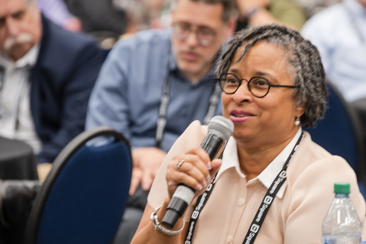 A woman, sitting in the audience, speaks into a microphone.