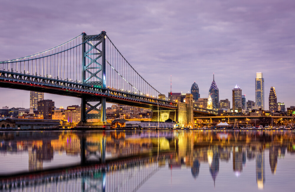 Waterfront view of the Ben Franklin bridge with illuminated Philadelphia skyline.