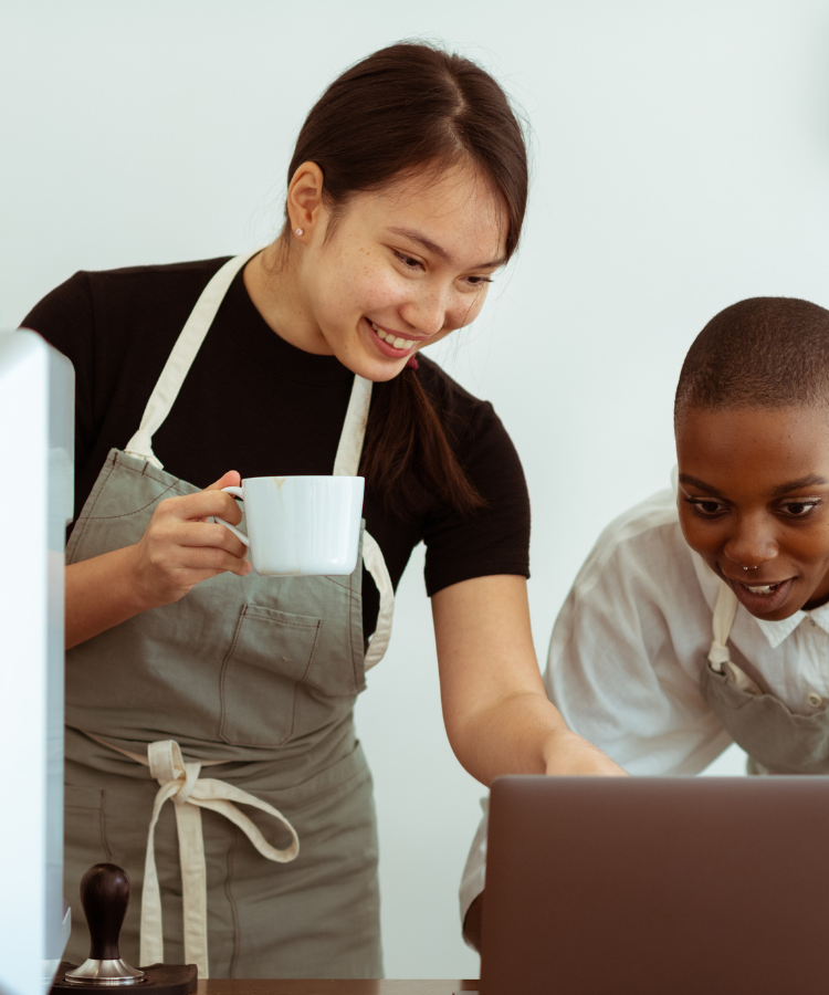 Two women working at coffee shop look at a computer screen.