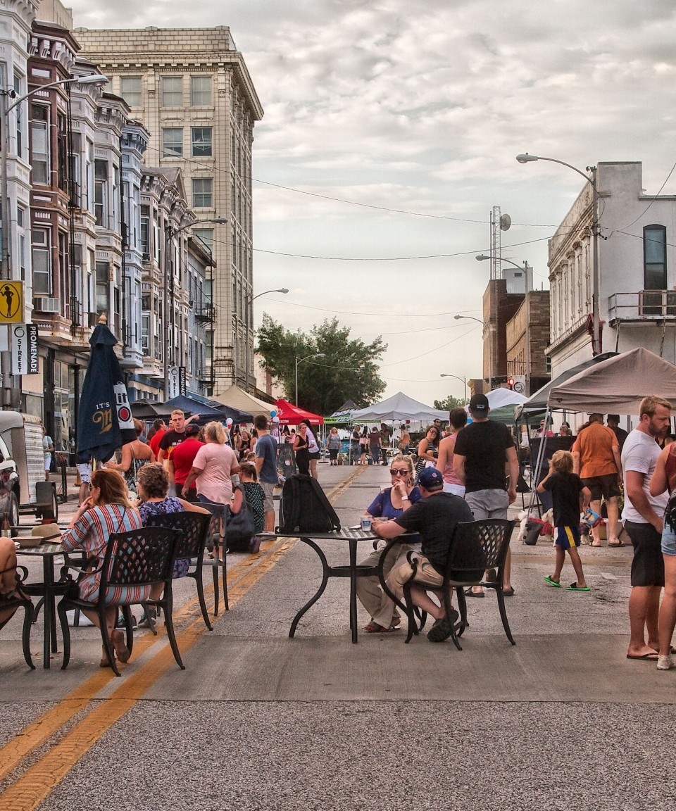 People gathering around tables and in groups at an open streets event.