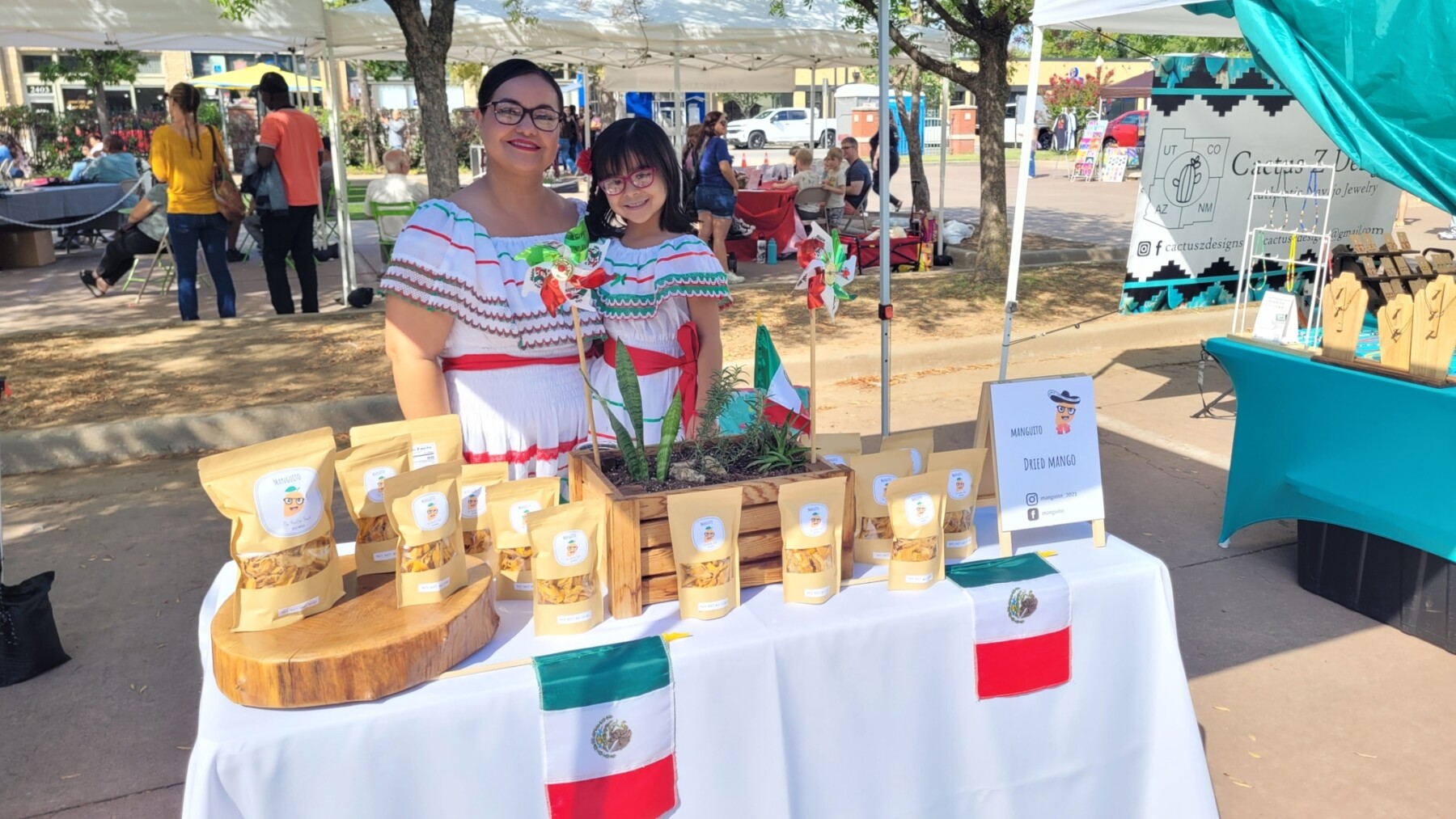 A woman and girl wearing traditional Mexican dresses sell dried mangos at an outdoor market