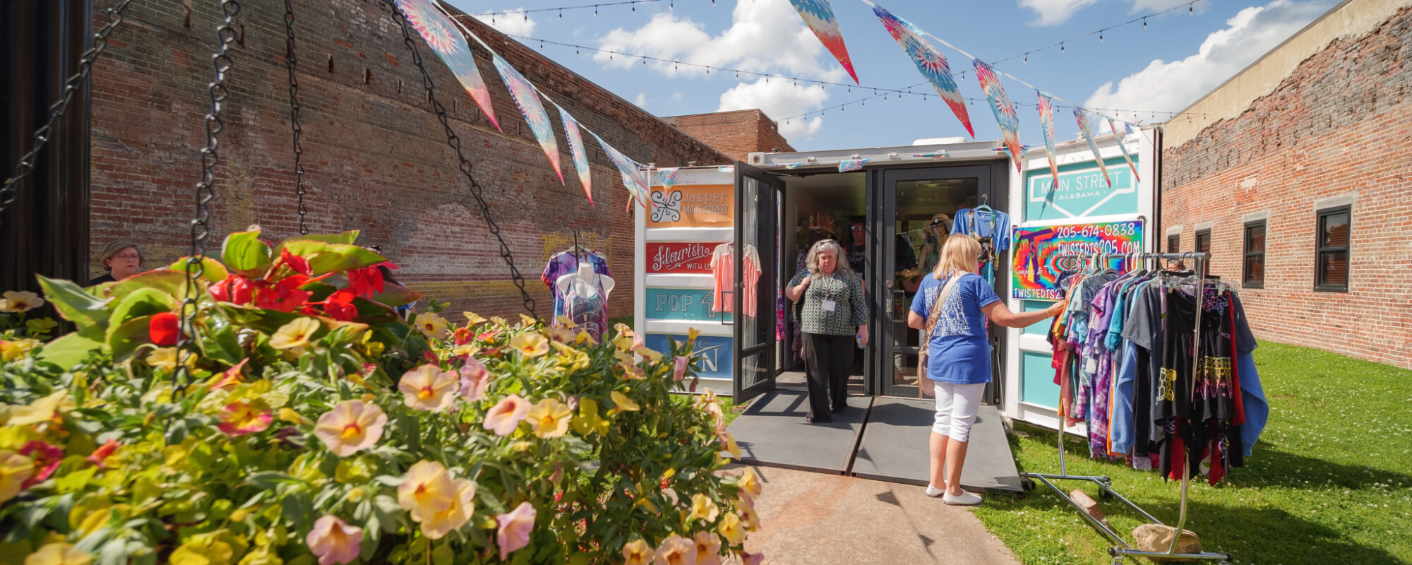 People shopping at a small retail store in a shipping container surrounded by flowers and colorful pennants