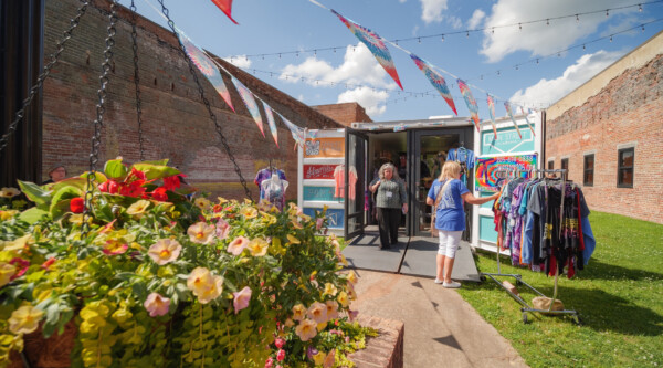People shopping at a small retail store in a shipping container surrounded by flowers and colorful pennants