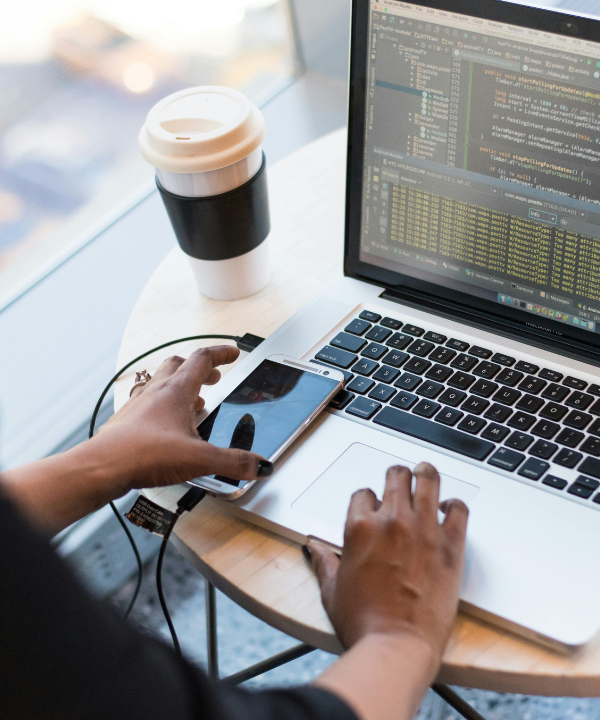 Woman working at a computer at a desk with coffee mug and glasses sitting on desk.