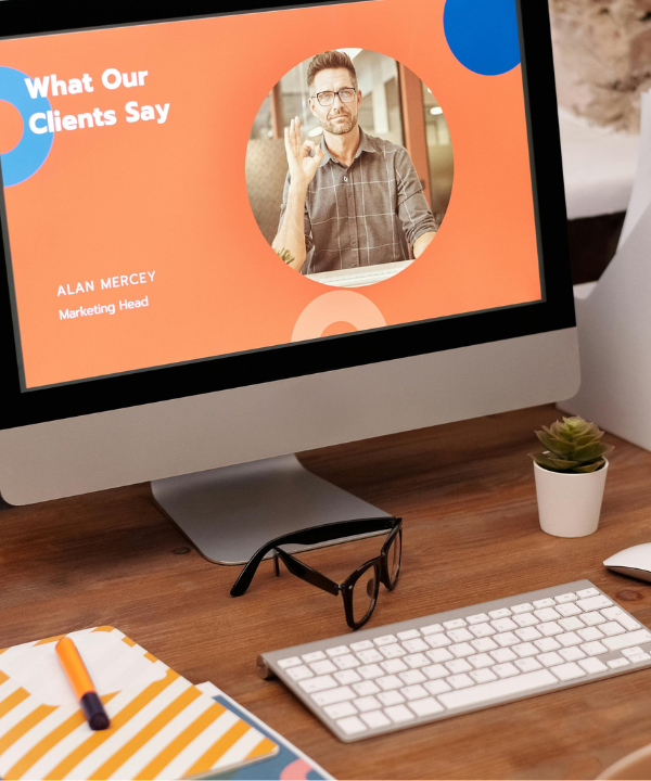 Computer showing a website sits on a desk with a keyboard, notebook, lamp, folders, and cup of coffee.