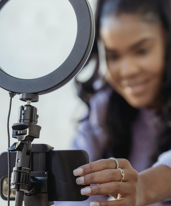 Woman wearing purple sweater positions camera on tripod with ring light attached.