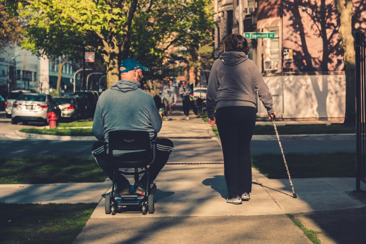 A person using a wheelchair and a person using a cane walk down a sidewalk in Chicago, Illinois.