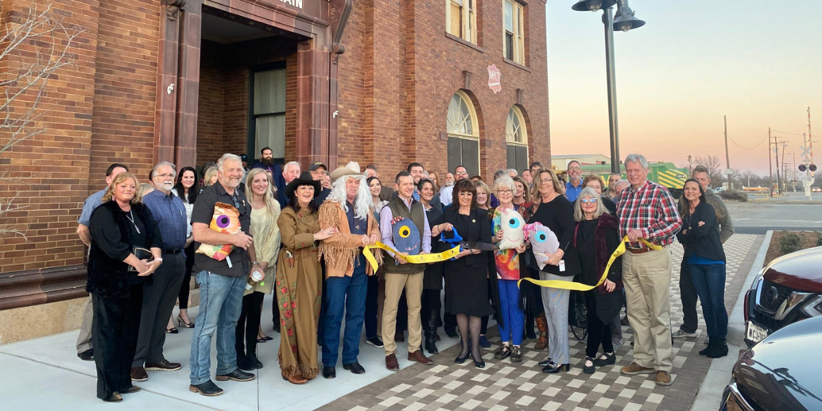 Group of people participating in a ribbon cutting outside a historic, red brick building