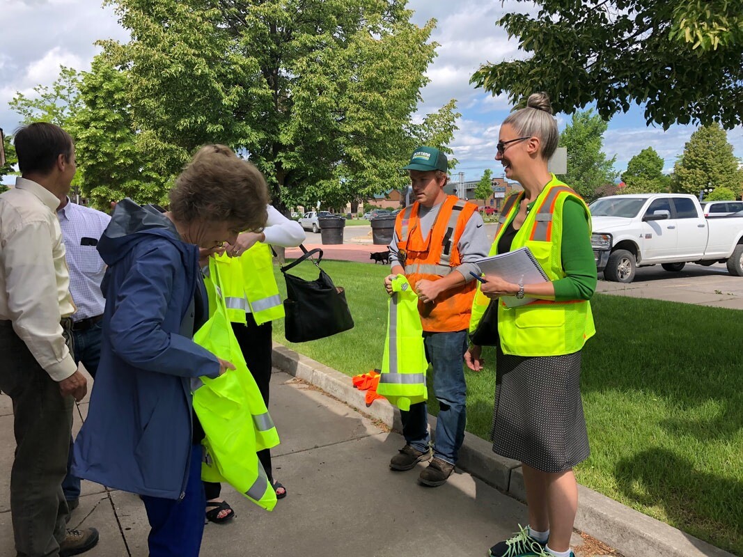 Committee members putting on fluorescent yellow vests while standing on a downtown sidewalk