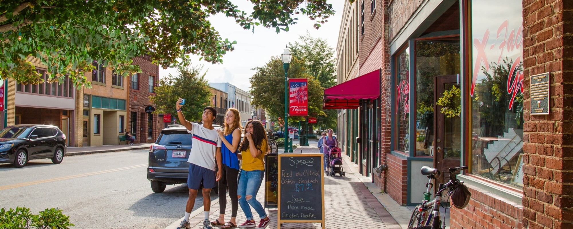 People pose for a selfie on a sunlit downtown street