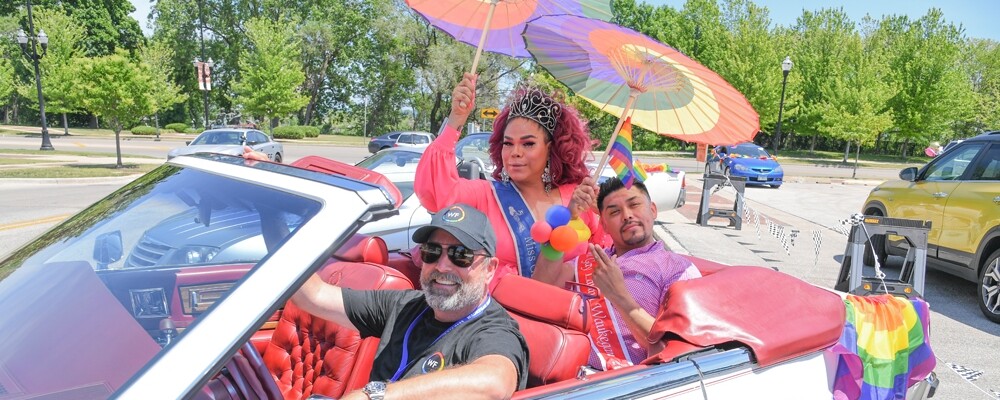 Waukegan pride event, people wearing rainbow attire riding in a car during a parade