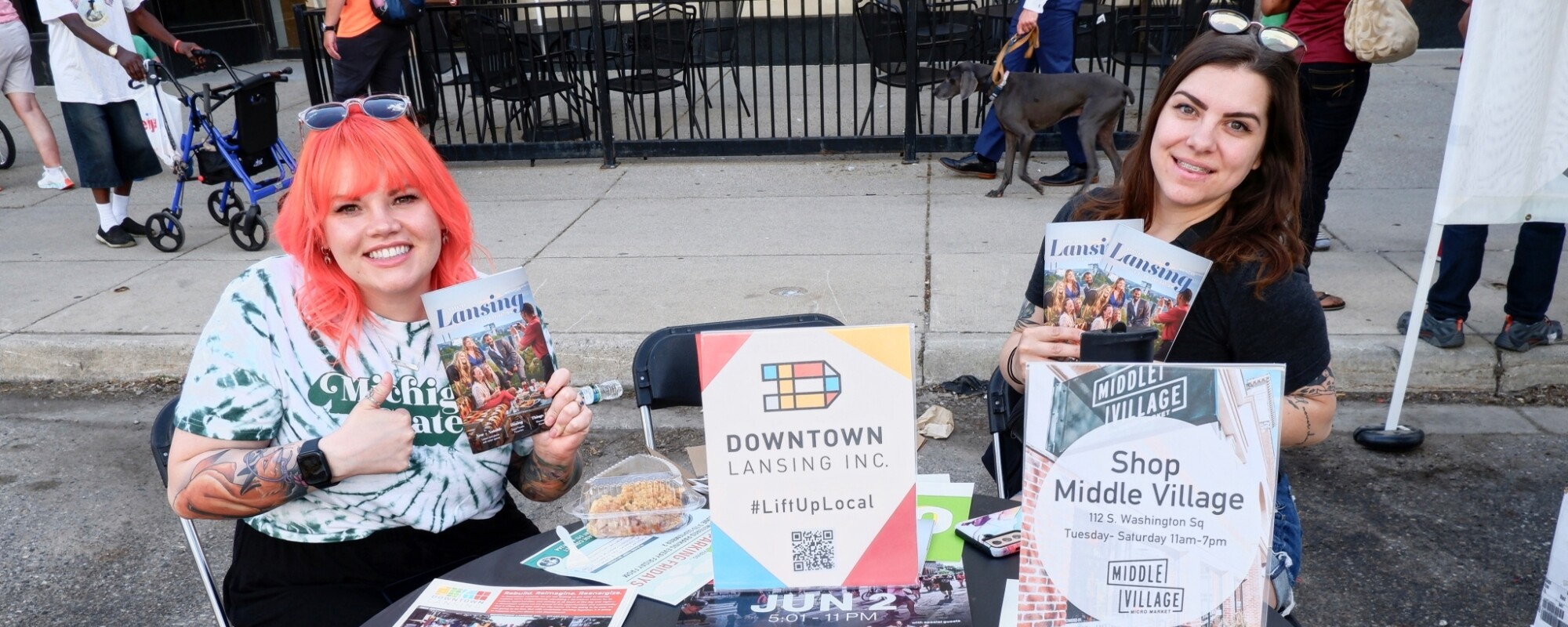 Volunteers in Lansing, Michigan, sitting at a table with promotional materials for Downtown Lansing