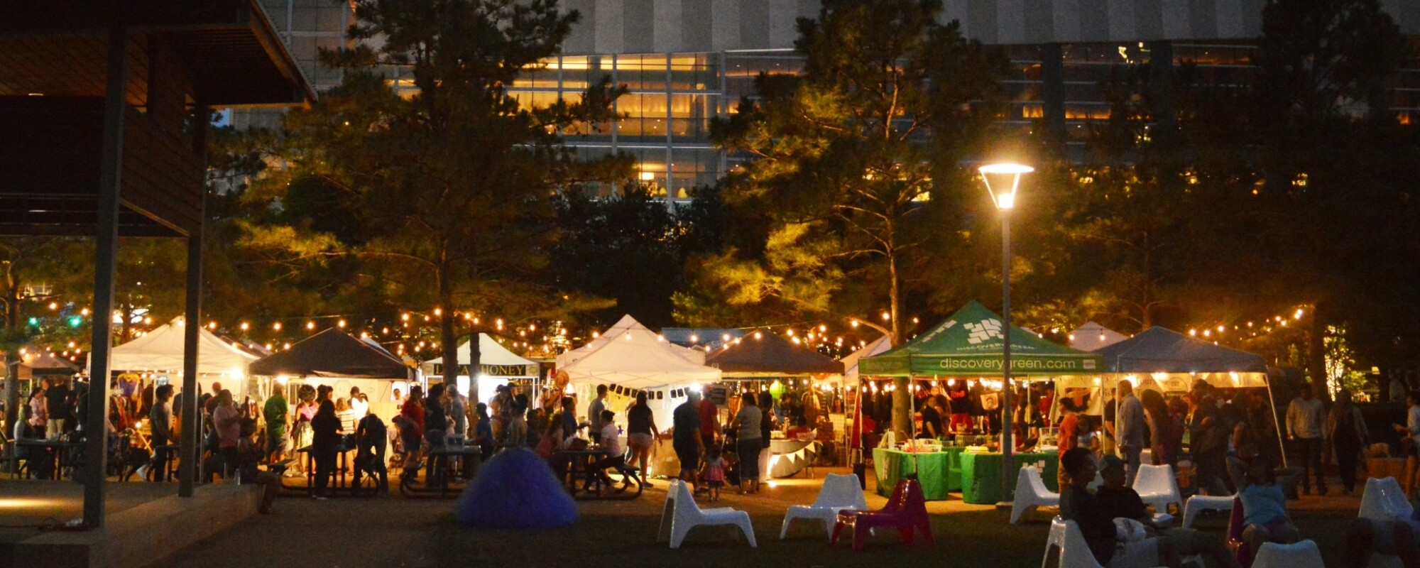 People sit at outdoor tables and shop at tents during a market in Discovery Green Park, Houston, Texas.