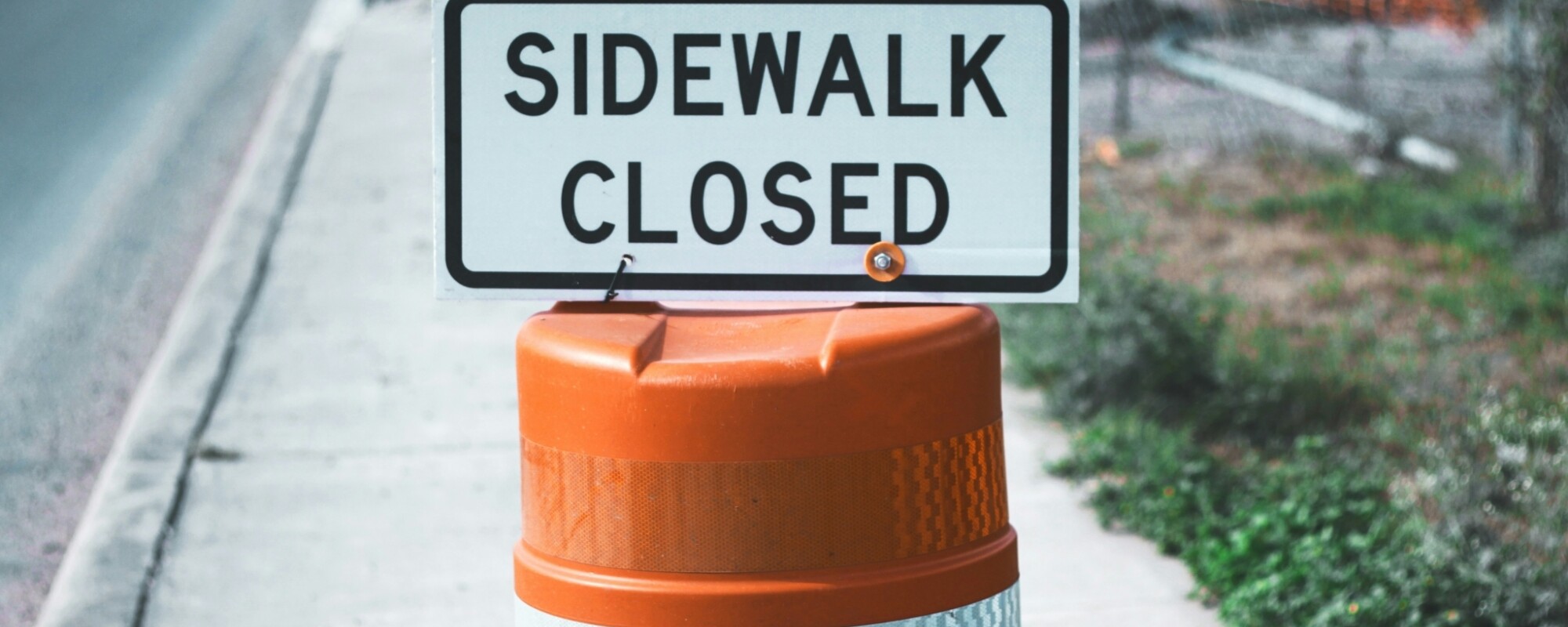 Orange cone holding a sign that says "sidewalk closed"