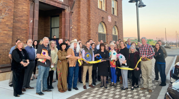 Group of people participating in a ribbon cutting outside a historic, red brick building