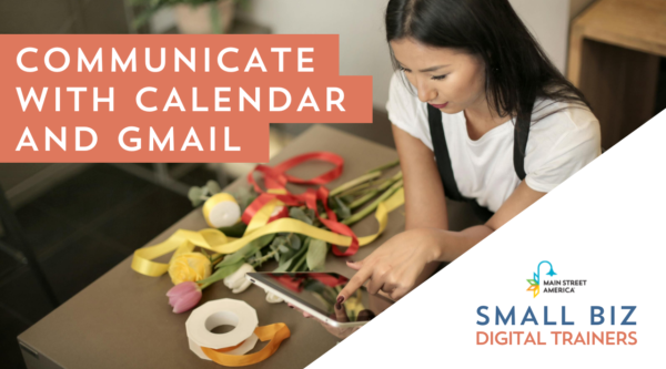 Woman with black hair wearing apron and leaning on work bench covered with floral arrangement supplies looks at ipad.