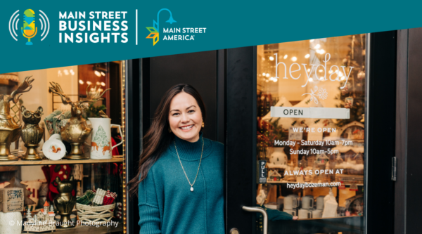 A woman wearing an emerald green sweater smiles while opening door to small boutique.