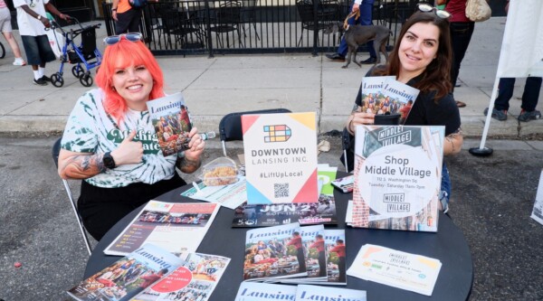 Volunteers in Lansing, Michigan, sitting at a table with promotional materials for Downtown Lansing