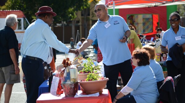 Two men shake hands at a community event information table.