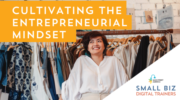 Mujer sonriente con camisa blanca delante de un perchero en un pequeño negocio. Las palabras delante de la imagen dicen: "Cultivating the Entrepreneurial Mindset" con el logo de Main Street America sobre las palabras: "Small Biz Digital Trainers".