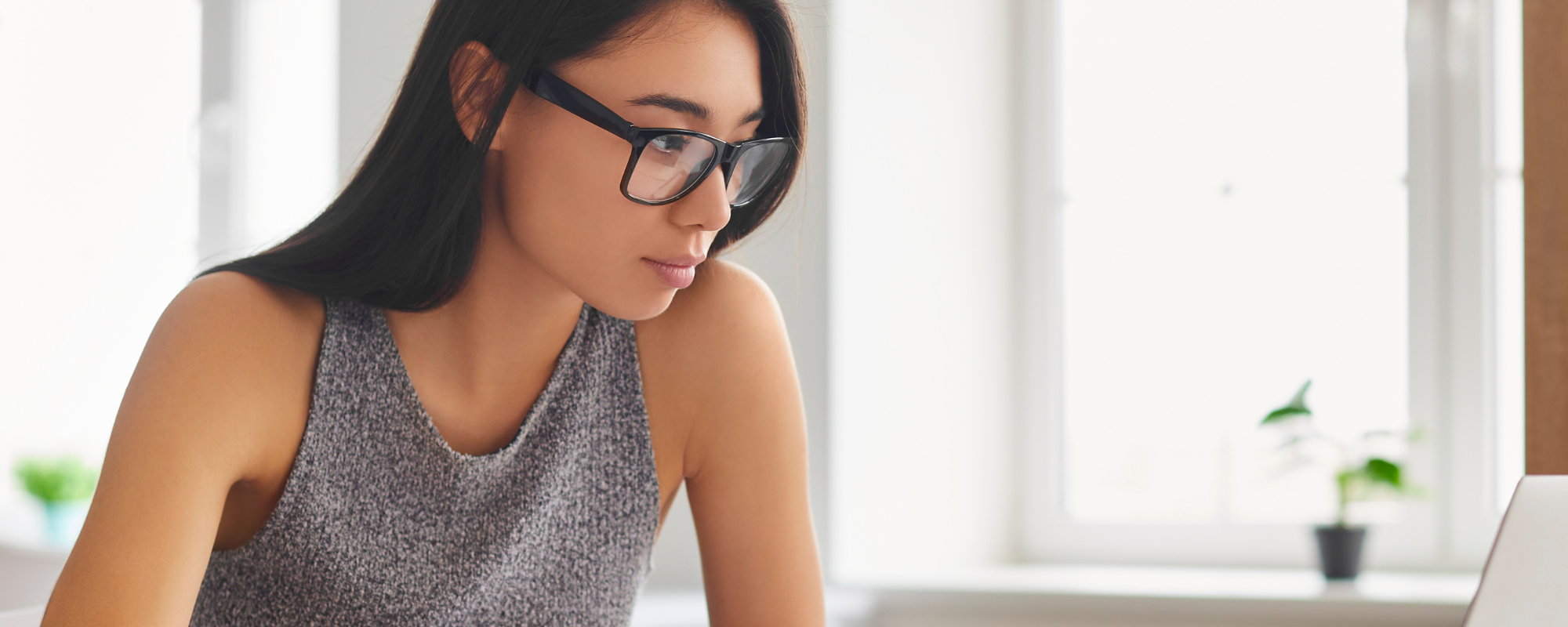 A young woman takes notes while studying at a laptop.