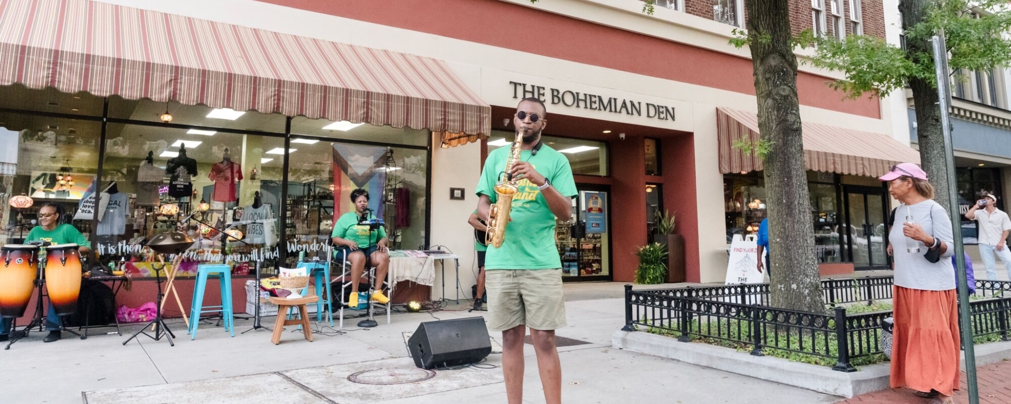 A saxophonist and vocalist perform on a sidewalk in front of a retail store.