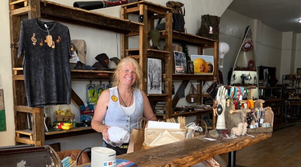 A woman smiles while standing behind a retail store counter and placing an item into a paper bag.