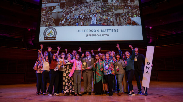 A group of people standing on a theater stage cheer.