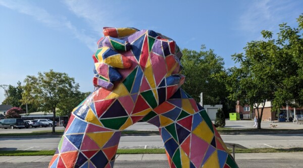 Large, multi-colored sculpture of hands rising up from the ground and clasping.