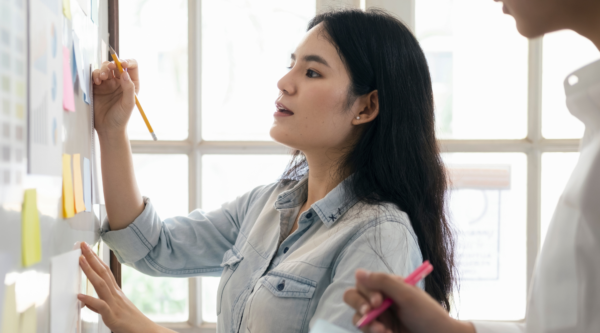 Two people brainstorming and discussing a project on a whiteboard.