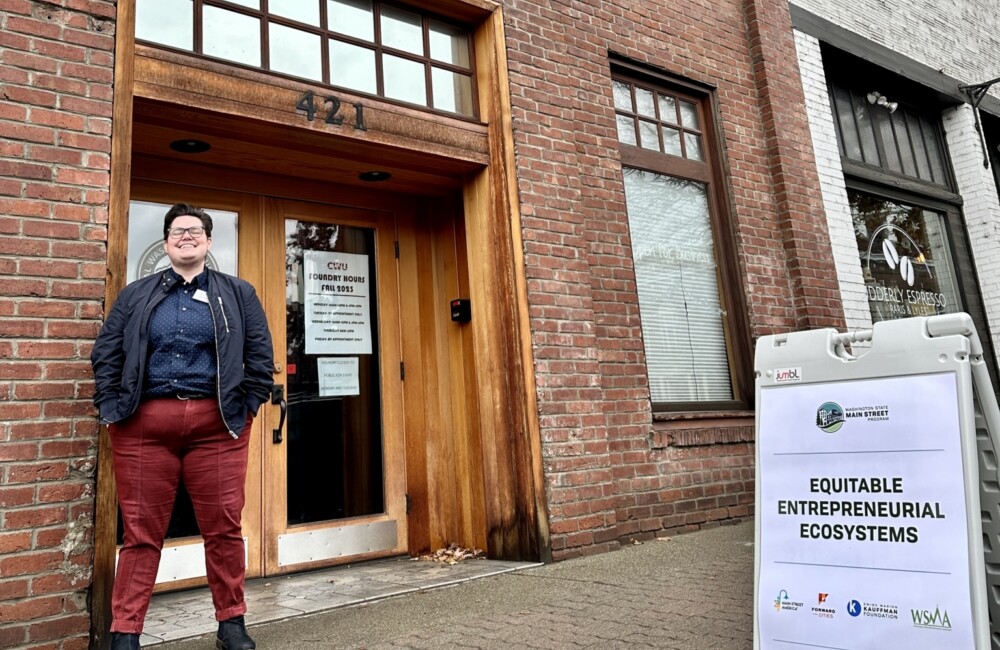 Tasha Sams poses in front of a brick building next to a sign reading "equitable entrepreneurial ecosystems"