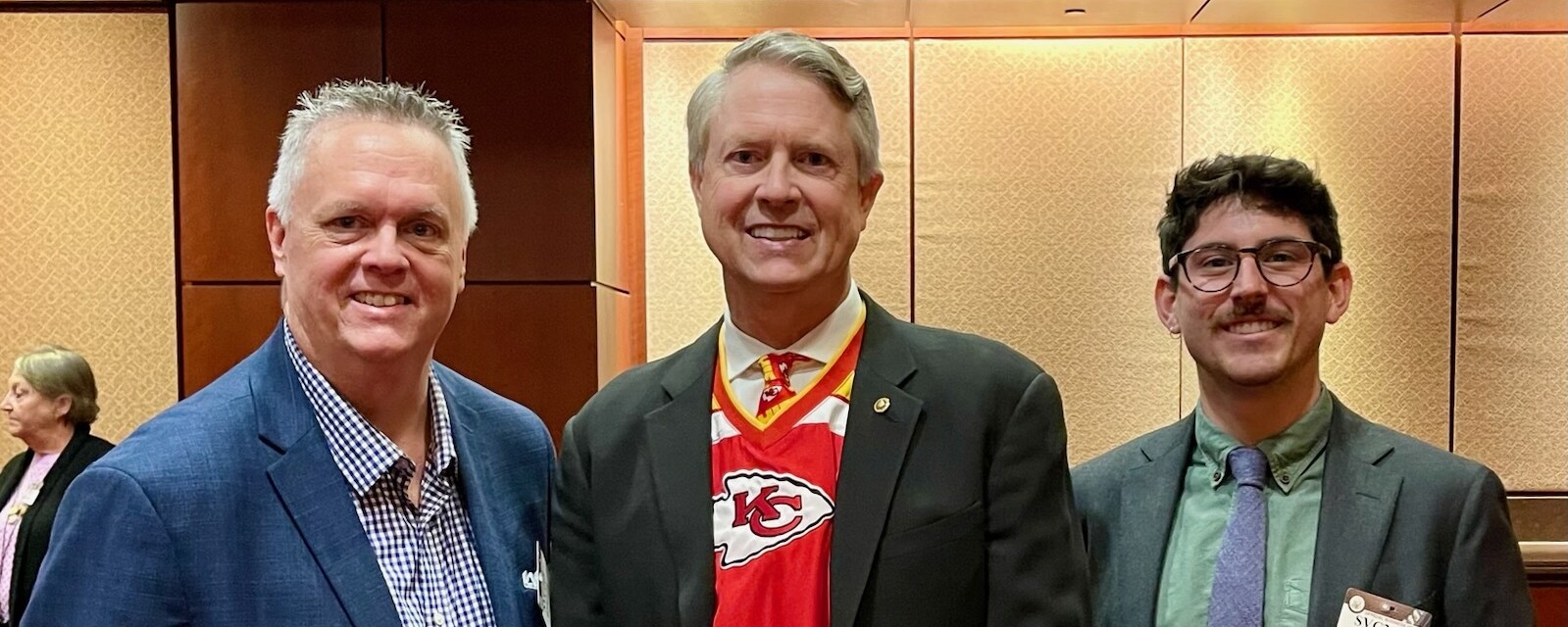 Three people pose, one wearing a Kansas City chiefs jersey