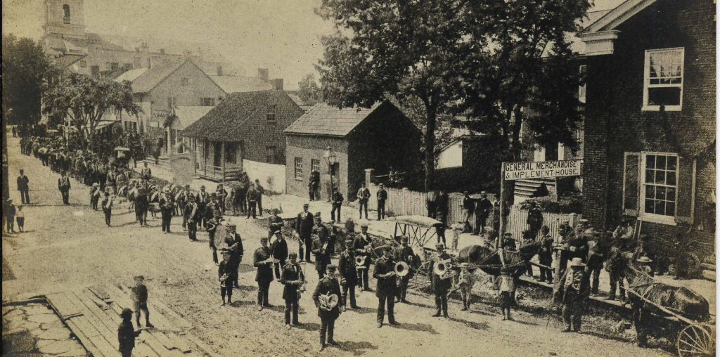 Historic black and white photo of Main Street in Middletown. People are walking past the downtown buildings during a parade.