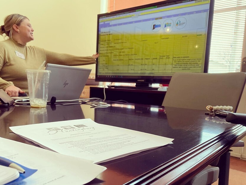Jackie Swihart sitting at a conference table pointing at data on a projector screen