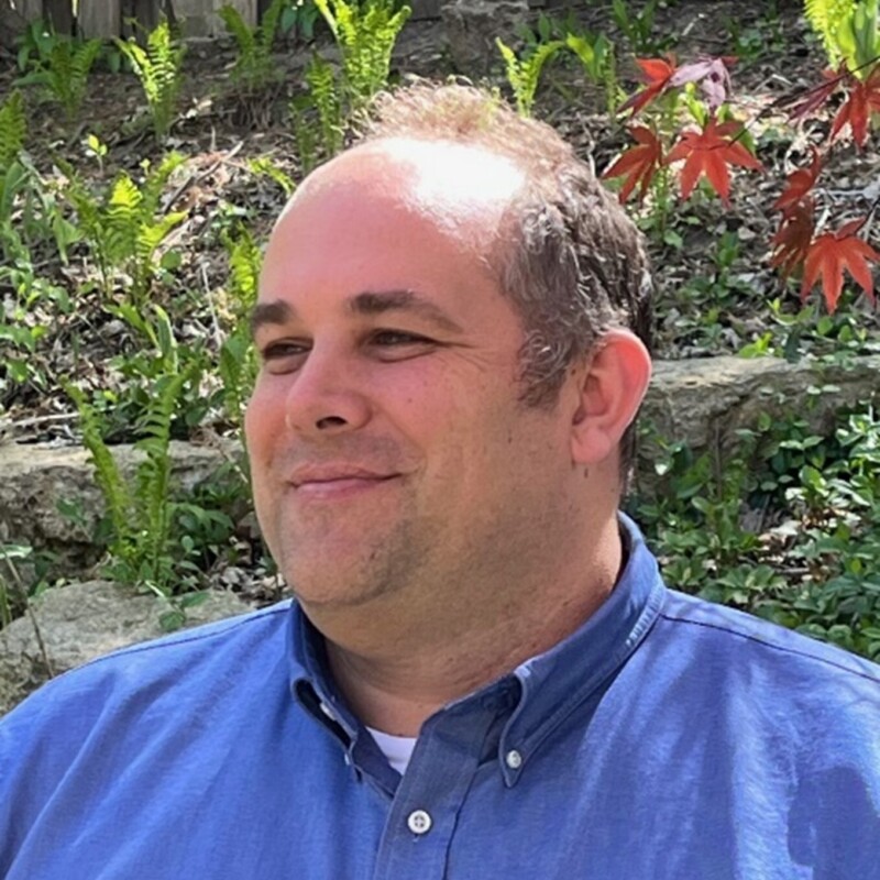 A photo of Brian Kramer standing in front of some greenery