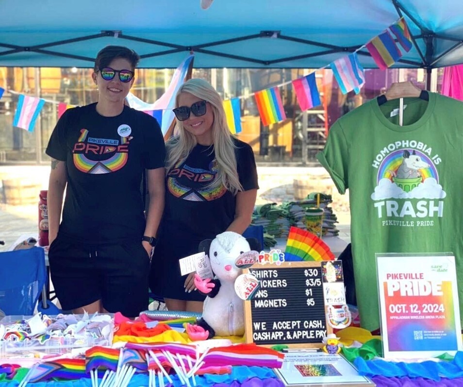 Two people wearing Pikeville Pride shirts selling merchandise at a booth during the pride event