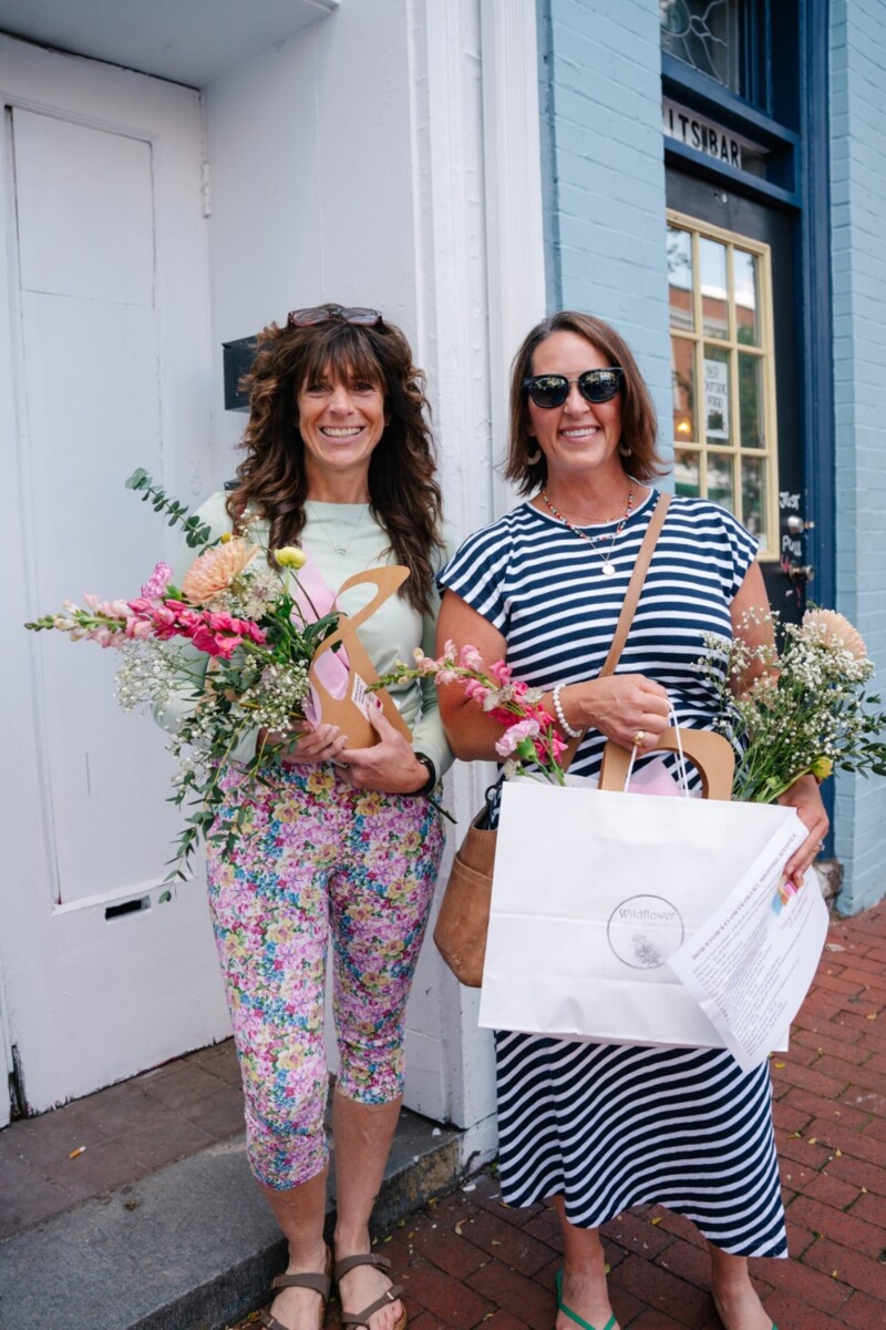 Two women holding bouquets of flowers and shopping bags