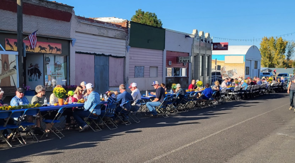 People sit at a long table on the street in a historic downtown