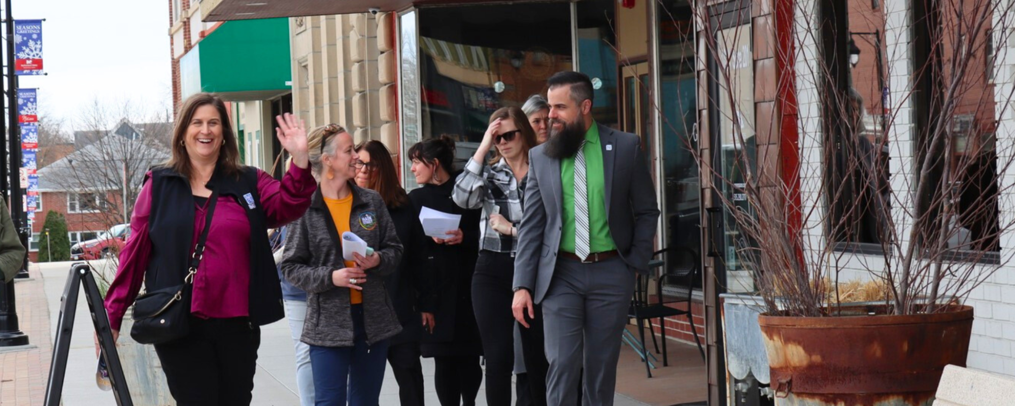 A small group of people walk down a sidewalk; one person smiles and waves while others engage in conversation.