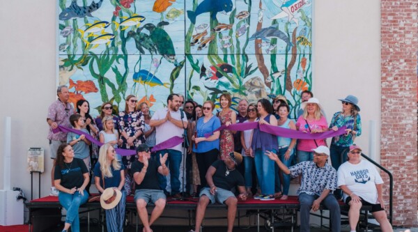 People pose during a ribbon cutting for a stained glass mural featuring sea creatures