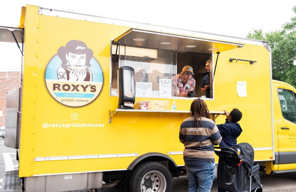 A woman and a boy place their orders at the counter of a yellow food truck